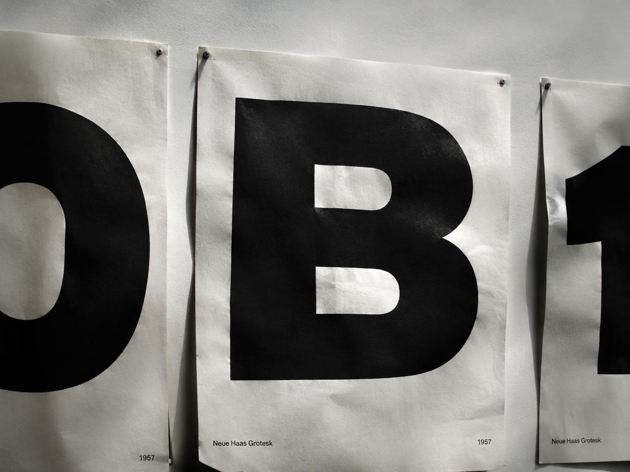 Large black grotesque letterform posters pinned to a white wall